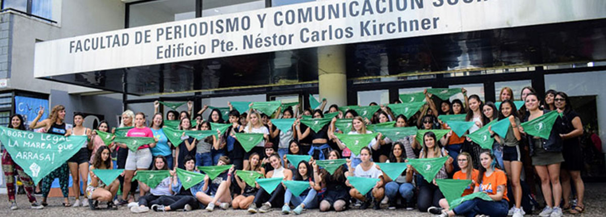 Un grupo de estudiantes y docentes posan frente a la entrada de la Facultad con pañuelos verdes