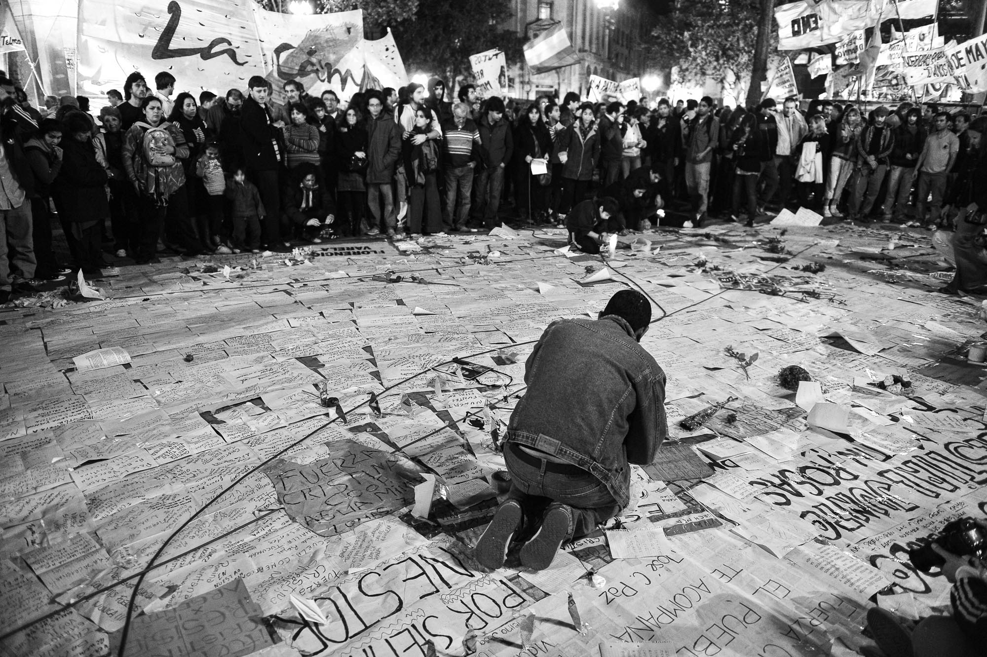 un hombre acomoda cientos de carteles con mensajes en el suelo rodeado de gente