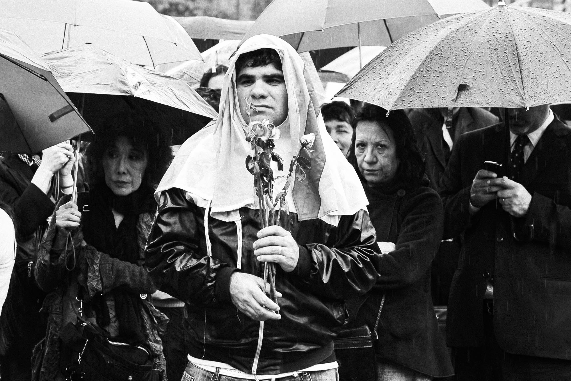 un hombre serio con rosas en sus manos delante de la multitud con paraguas