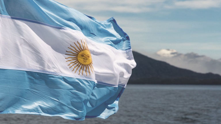 Bandera argentina sobre flameando, detrás agua y montañas