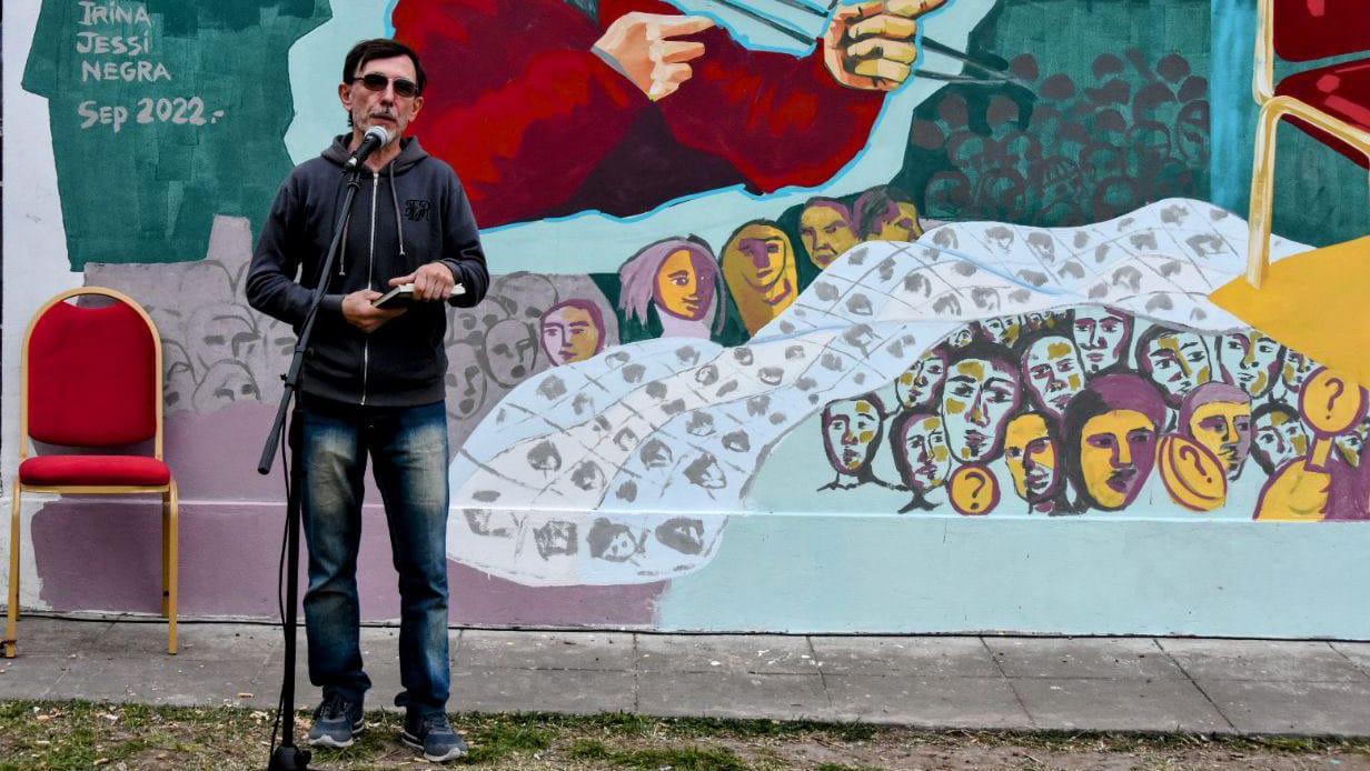 persona hablando frente a un microfono, detrás de él un mural que recuerda a Jorge Julio López