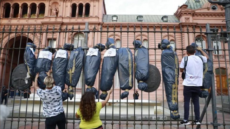 bolsas mortuorias y tres personas frente a la Casa Rosada