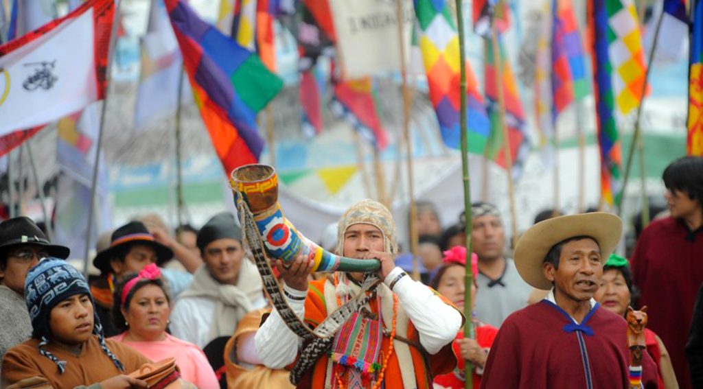 personas de pueblos originarios con banderas y tocando el didgeridoo