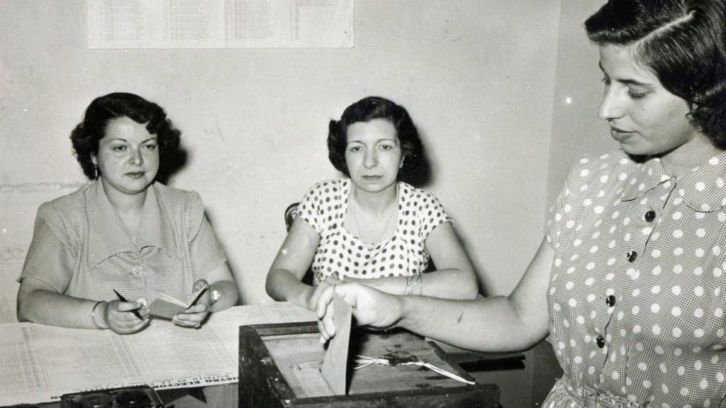 Tres mujeres y una de ellas colocando un sobre en una urna